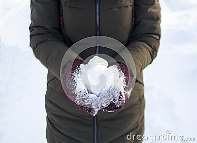 One person holds a snowball in winter in the Park, walk, fun, sports and leisure, green jacket, Burgundy mittens Stock Photo