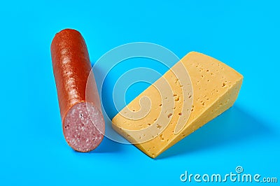 One piece of cheese in form of triangle near half of long sausage lies on blue desk on kitchen or market Stock Photo