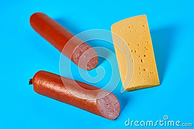 One piece of cheese in form of triangle near two halves of long sausage lies on blue desk on kitchen or market Stock Photo