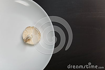 One raw champignon mushroom on a white plate on black table. Not enought food or oversaturation concept. Diet, nutrition Stock Photo