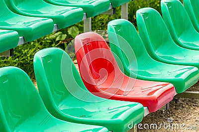 One red seat among different color green seats in a stadium Stock Photo