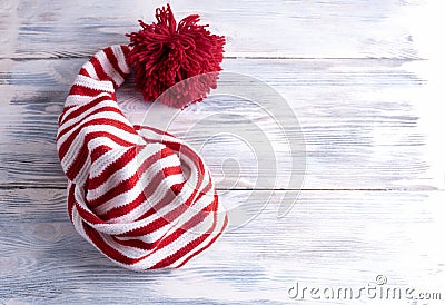 One red and white striped cap with a long tail and a large red pompom is on a white wooden background Stock Photo