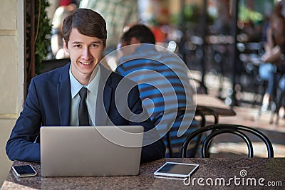 One relaxed young handsome professional businessman working with his laptop, phone and tablet in a noisy cafe. Stock Photo