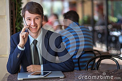 One relaxed young handsome professional businessman working with his laptop, phone and tablet in a noisy cafe. Stock Photo