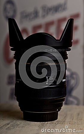 Camera lens standing against a wall with the word `coffee` written and out of focus. Editorial Stock Photo