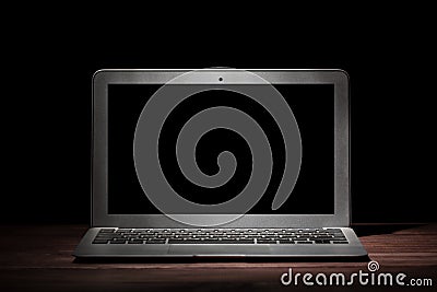 One silver modern laptop on wooden table in a dark room on black background. Nice mockup for your IT project. Dramatic light. Editorial Stock Photo