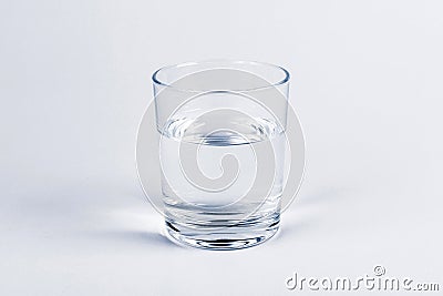 One simple half full half empty glass of fresh crystal clear clean drinking water, solo object isolated on light blue background Stock Photo