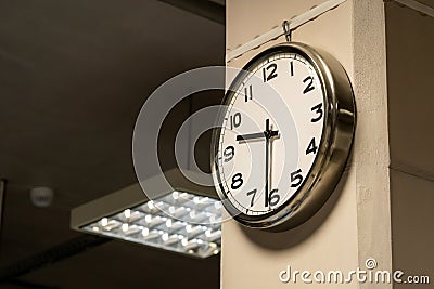One single simple industrial clock in a factory hall or a corporate office on the wall. Working 9 to 5, clocking in and out, time Stock Photo