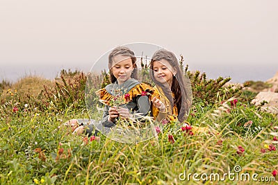 One sister gives another red flower sitting near the bushes on the grass and dressed in vintage clothes dress Stock Photo