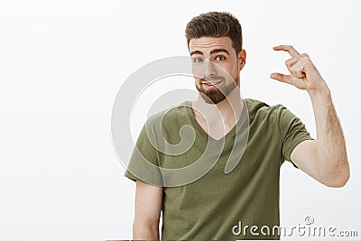 One small shot shall we. Handsome adult bearded guy in olive t-shirt shaping tiny or little thing and looking questioned Stock Photo