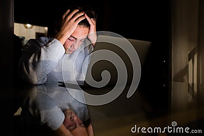 One teenager or millennial working or studying at late night for school or work - man tired of using his laptop after all day at Stock Photo