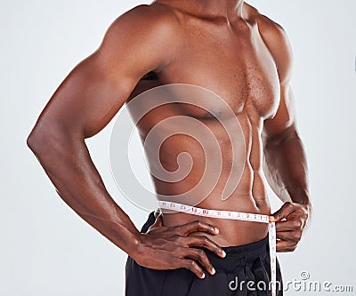 One unrecognizable African American fitness model posing topless with tape measure around his waist while looking Stock Photo