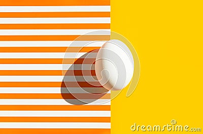 One white egg on duotone yellow orange and white striped background. Easter concept. Hard light harsh shadow. Trendy minimalist Stock Photo