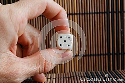One white plastic dices in man`s hand on brown wooden table background. Six sides cube with black dots. Number 5 Stock Photo