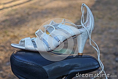 one white womens leather high heel sandal standing on a black bicycle saddle Stock Photo