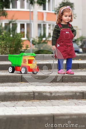 One year old curly girl pulling a truck trying to surmount an obstacle of steps Stock Photo
