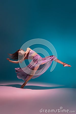 One young flexible contemp dancer in lilac dress dancing isolated on gradient blue white background in neon. Stock Photo