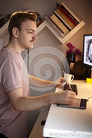 One young man, 20-29 years old, upper body shot, working at his desk at home, with graphic tablet and wireless keyboard, looking t Stock Photo