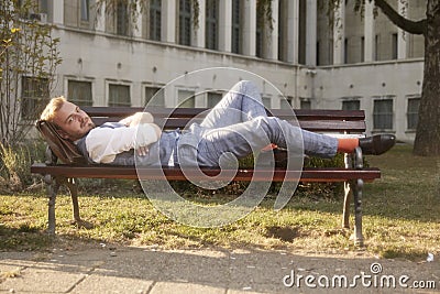 One young smiling man, 20-29 years old, wearing hipster retro suit, laying on bench in park Stock Photo