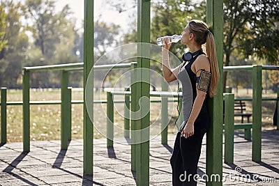 One young woman, drinking from water bottle, outdoors gym in park, r Stock Photo