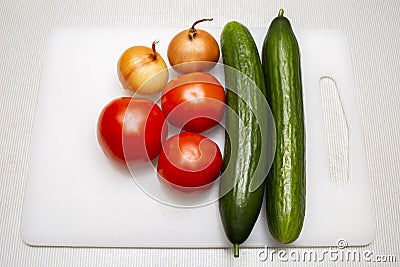 Onion heads, fresh tomatoes and cucumbers on cutting board Stock Photo