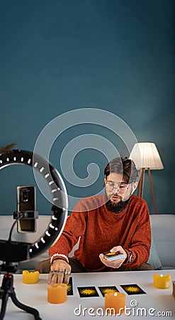 Online astrology. Male fortune teller is use a smartphone, reads tarot cards for predictions, telling customers by Stock Photo