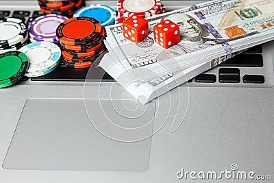 Online casino laptop. Laptop keyboard and chips with dice and money cash dollars on green gaming table. Game addiction gambling Stock Photo