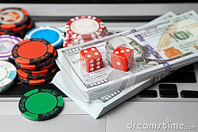 Online casino laptop. Laptop keyboard and chips with dice and money cash dollars on green gaming table. Game addiction gambling Stock Photo