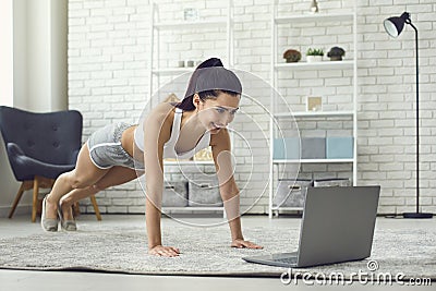 Online home sports. Young fit woman exercising to video tutorial indoors, doing plank or push up exercise Stock Photo