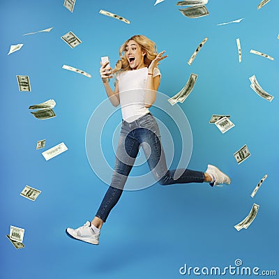 Online Lottery. Overjoyed Woman Jumping With Smartphone Under Money Shower, Celebrating Victory Stock Photo