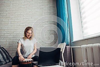 Online music lessons during quarantine due to coronavirus pandemic. Remote teaching to play the drum. Young woman watches video Stock Photo