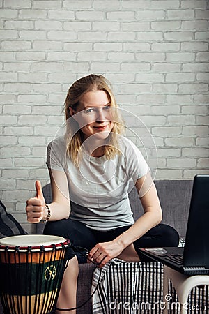 Online music lessons during quarantine due to coronavirus pandemic. Remote teaching to play the drum. Young woman watches video Stock Photo