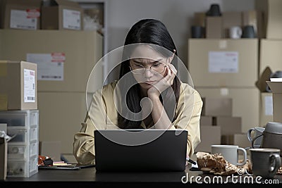 Online seller entrepreneur in a warehouse looking at laptop and worrying about e-commerce business due to lack of sales Stock Photo