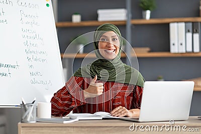 Islamic teacher in headscarf sitting at desk showing thumbs up Stock Photo