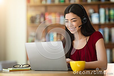 Online Tutoring. Asian Woman Tutor With Headset Working On Laptop In Cafe Stock Photo