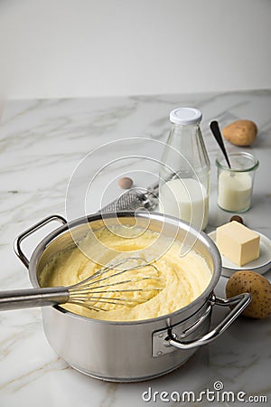 Ooking pot with mashed potatoes and ingredients as potato, milk, salt, butter, nutmeg with whisker and grinder on light marble Stock Photo