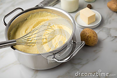 Ooking pot with mashed potatoes and ingredients as potato, milk, salt, butter, nutmeg with whisker and grinder on light marble Stock Photo