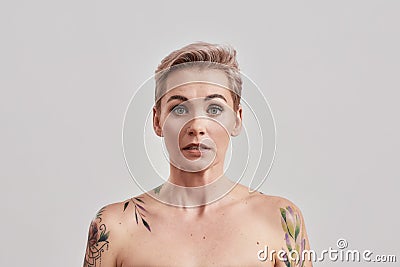 Oops. Portrait of half naked tattooed woman with short hair feeling awkward, silly isolated over light background Stock Photo
