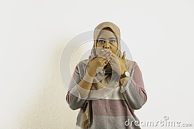 Oops! Surprised Asian Muslim woman wearing hijab or headscarf, with straight face covering her mouth with hands Stock Photo