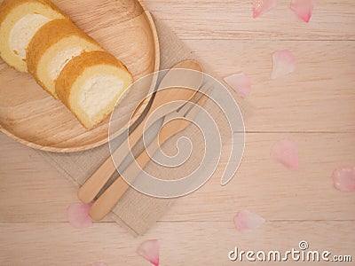 Op view vanilla cake roll on wooden dish with wooden spoon,fork,pink flower petals on beige wooden background Stock Photo