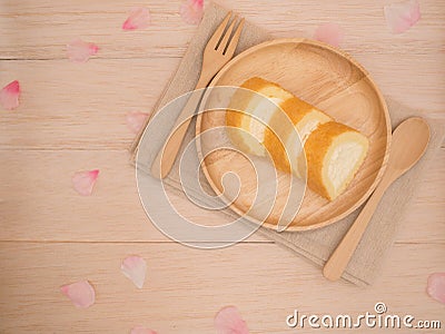 Op view vanilla cake roll on wooden dish with wooden spoon,fork,pink flower petals on wooden background Stock Photo