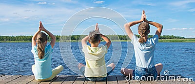 In the open air, on the pier, near the water the company of children is engaged in relaxation in the form of yoga Stock Photo