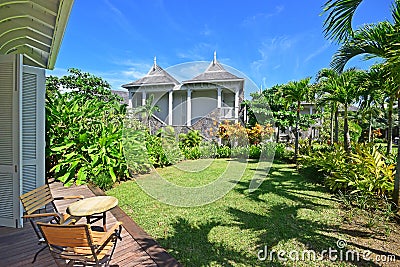 Room view of an open air porch with slightly extended roof and tall full length wooden door overlooking beautiful green garden Stock Photo