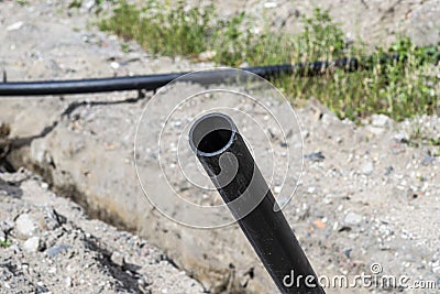 Open beginning of the plastic water pipe lying along the ditch with high groundwater, water connection in the housing estate. Stock Photo