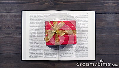 Open Bible. Book. Gift in a red package with a gold bow. On a wooden table. Stock Photo