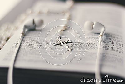 A bible is placed open on a table with a cross and ear buds. Stock Photo