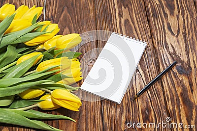 Open blank notebook and a bouquet of yellow tulips on a wooden table, top view. Women`s work Desk. The eighth of March. Holiday. Stock Photo