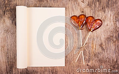 Open book with blank page and two lollipop in the shape of a heart on an old wooden table Stock Photo