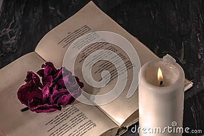 An open book with a candle. on the pages is a Bud of dried rose. Stock Photo