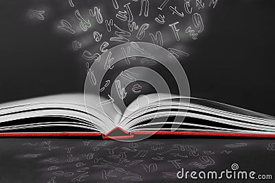 Open book with flying letters on black background. Dyslexia concept Stock Photo